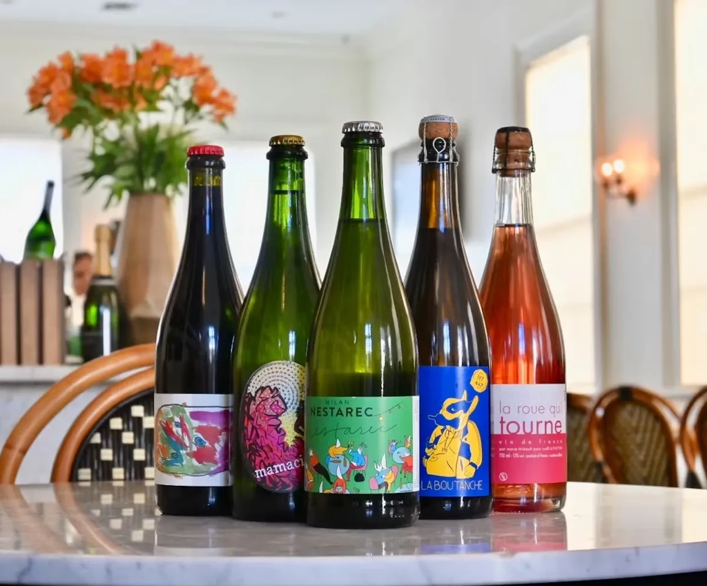 Five distinct natural wine bottles with colorful labels on a marble table.