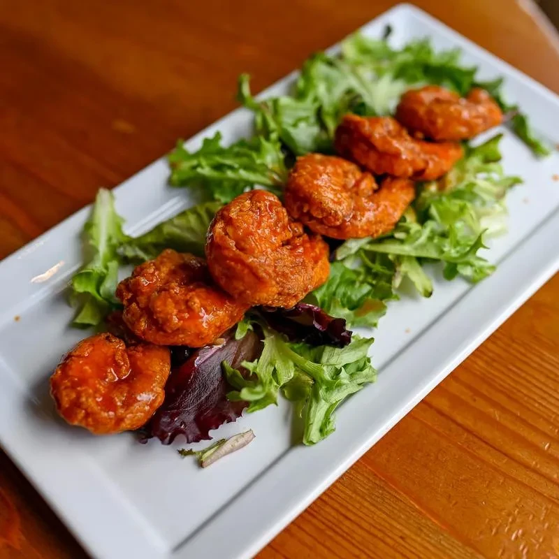 Battered shrimp or chicken in buffalo sauce, greens, white plate.