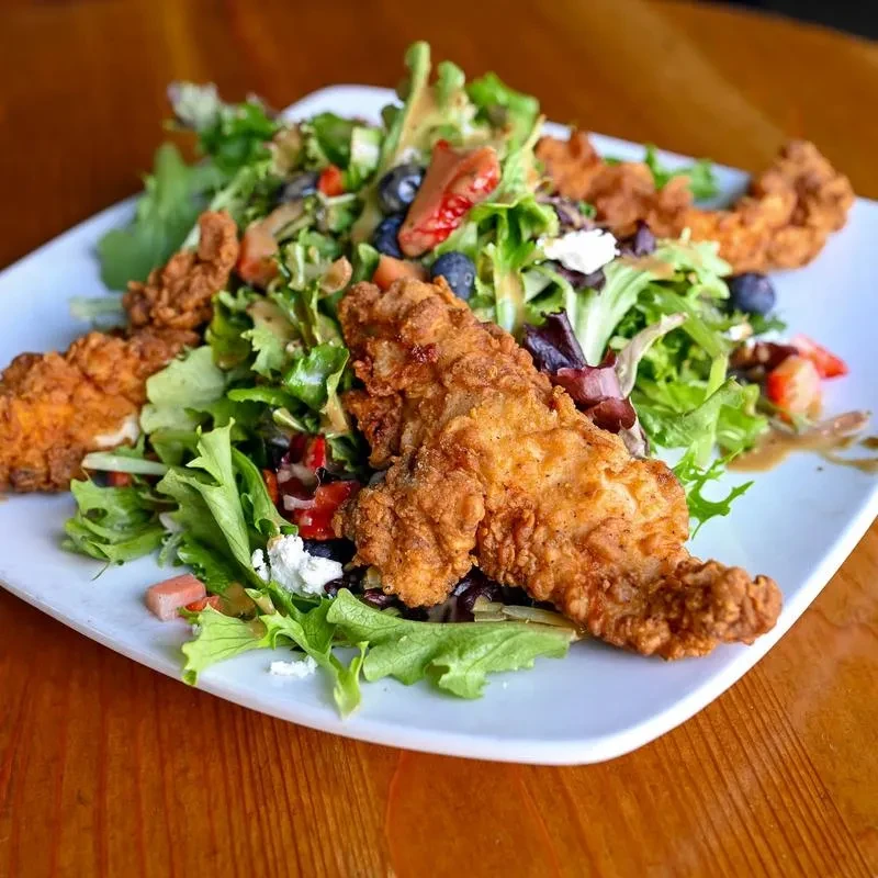 Fresh salad topped with crispy fried chicken, berries, and crumbled cheese.