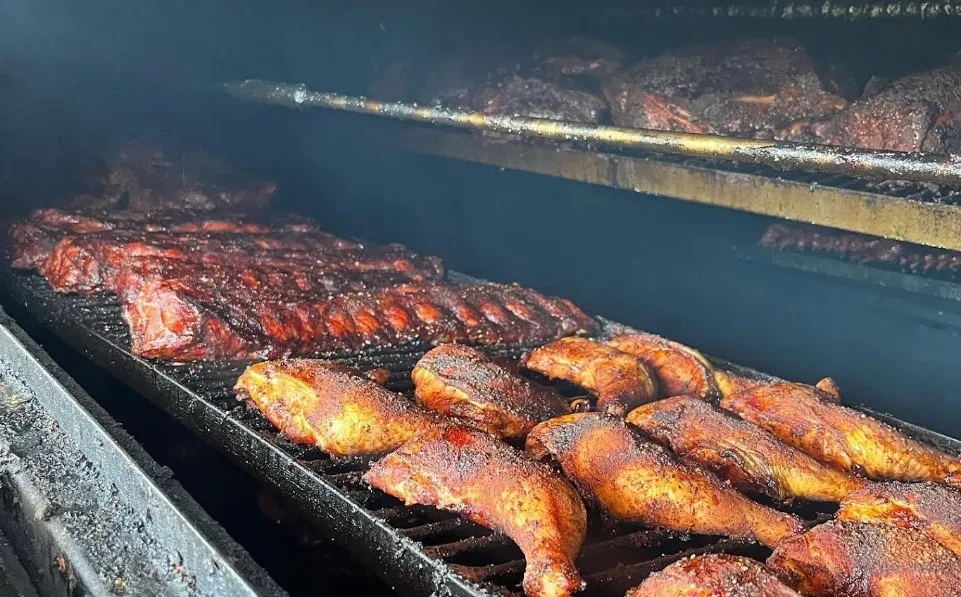 Close-up of seasoned BBQ ribs and chicken cooking inside a dark smoker.
