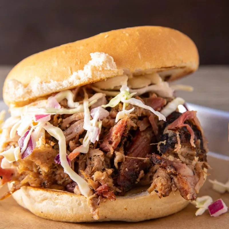 Generously portioned pulled pork sandwich with colorful coleslaw on a golden bun.