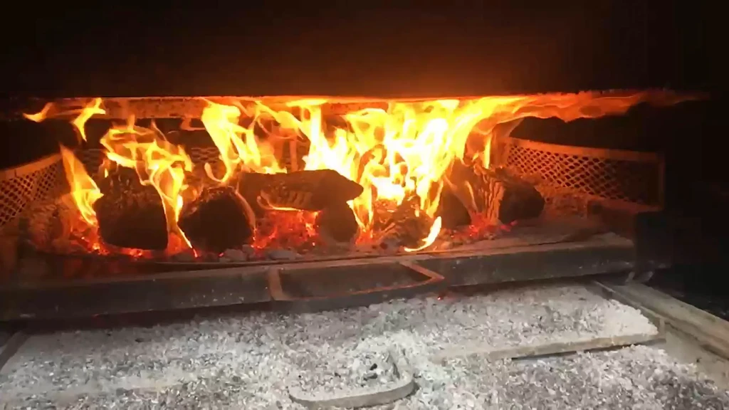Bright, roaring fire with glowing logs and ash inside a fireplace.
