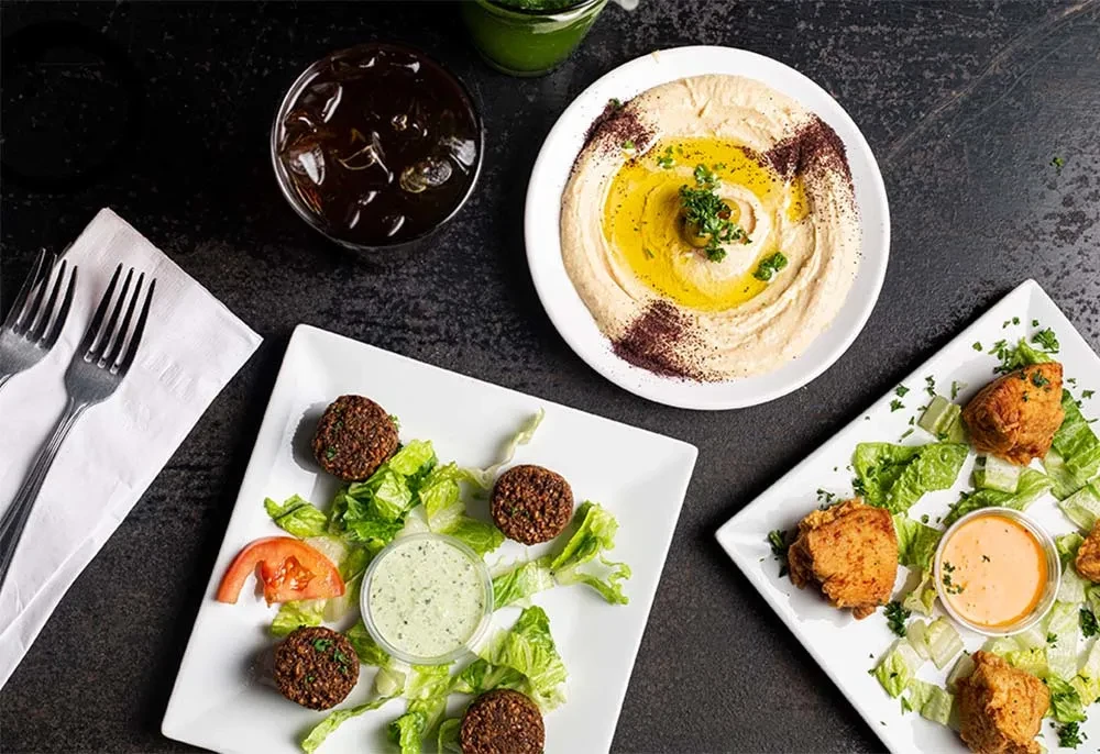 Overhead shot of hummus, falafel, and fried chicken dishes with drinks.
