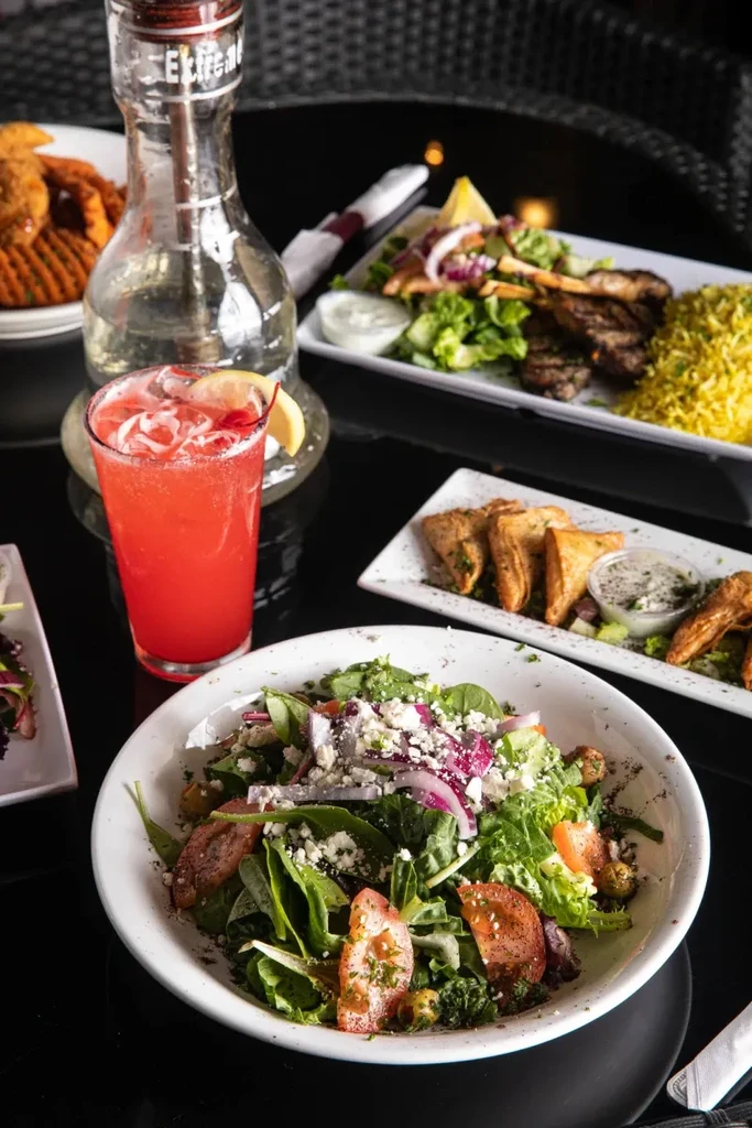 Overhead table view of salad, cocktail, hookah, grilled meat, and pastries.