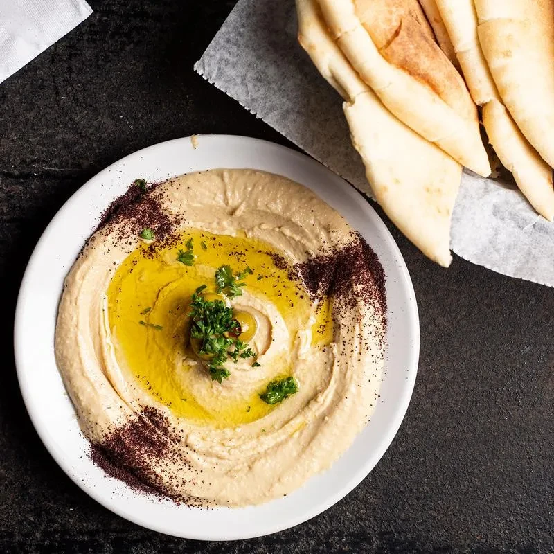 Overhead: Hummus with olive oil, spices, herbs, green olive, and pita.