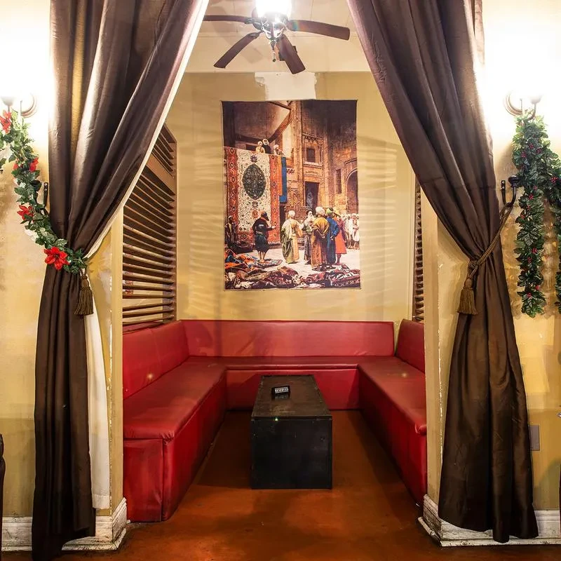 Red booth, coffee table, garlands, and marketplace tapestry in a restaurant.