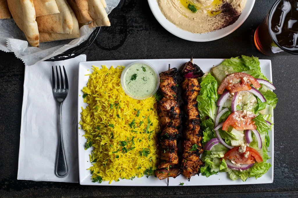 Colorful, top-down Middle Eastern meal with chicken, rice, hummus, salad.