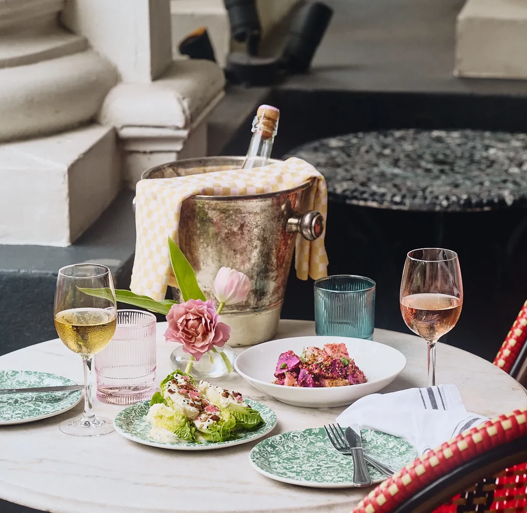 Two plated dishes, wines, and flowers on an outdoor marble table.