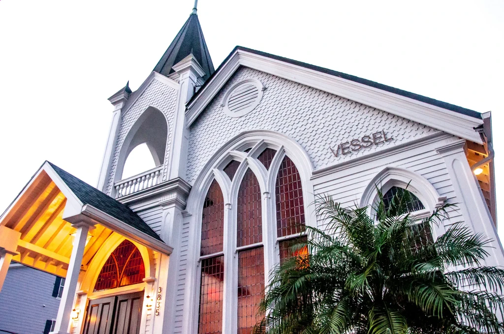 Ornate white church-like building, 'VESSEL' sign, steeple, palm tree.