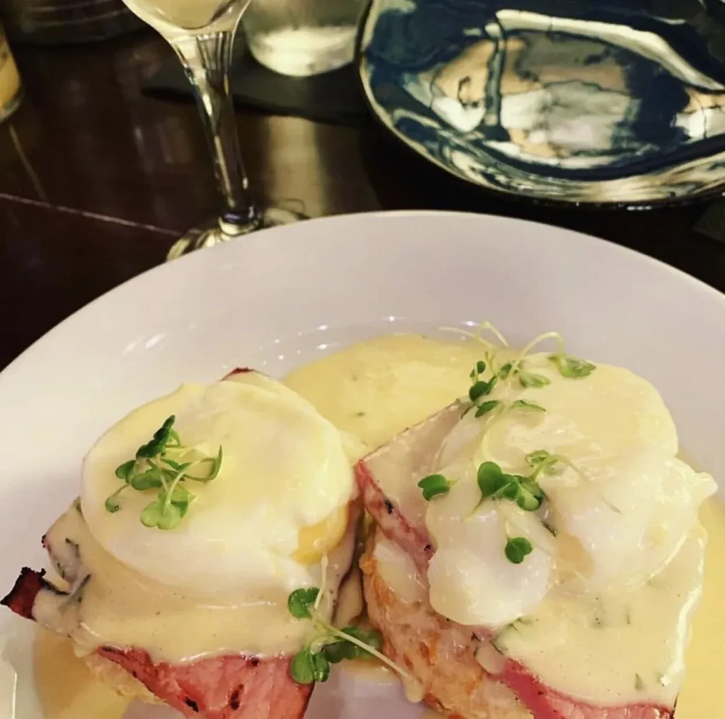 Two servings of Eggs Benedict garnished with hollandaise and microgreens.