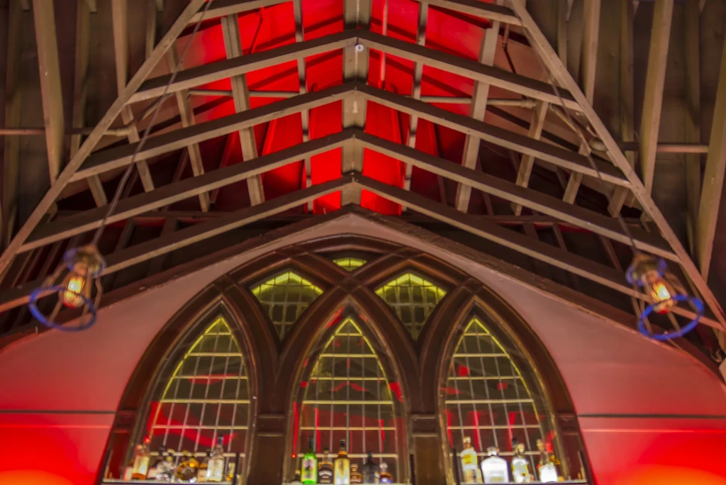 Bar interior with arched windows, liquor bottles, red-lit vaulted ceiling.