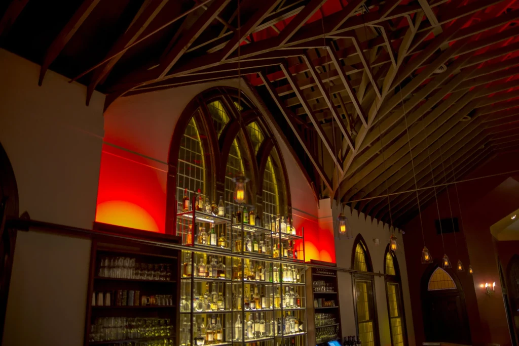 Elaborate bar with backlit spirits, arched windows, and an exposed wooden truss ceiling.