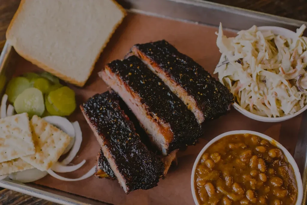 Full platter of smoked ribs with coleslaw, baked beans, and pickles.
