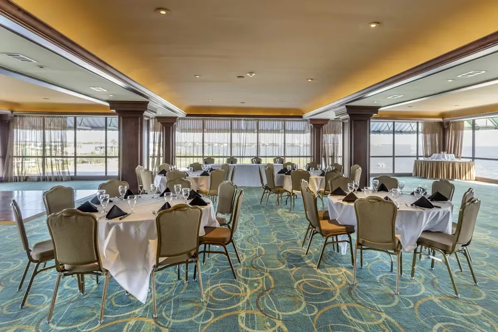 Spacious banquet hall with set tables, patterned carpet, and ocean view.