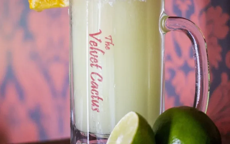 Close-up frosty green drink in "The Velvet Cactus" mug, limes.