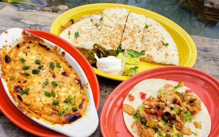 Three food dishes: baked dip, quesadillas, and a taco outdoors.