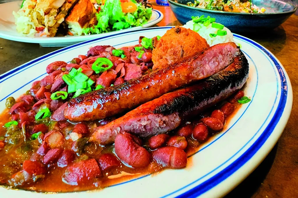 Grilled sausages, saucy beans, rice, and a fried fritter on a plate.