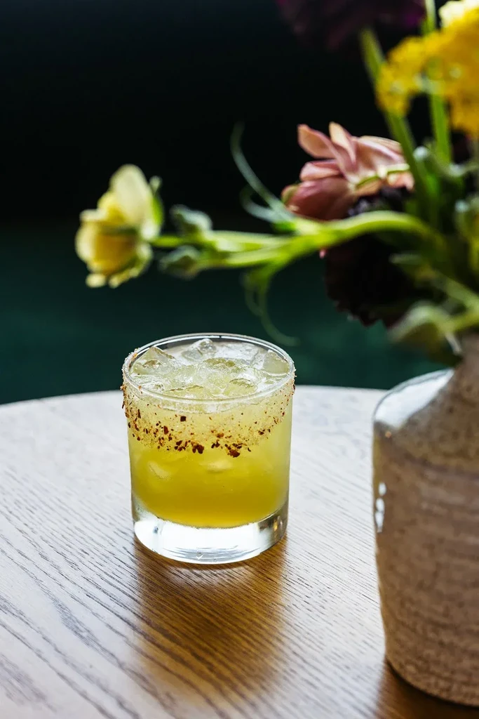 Spiced-rimmed yellowish-green cocktail with ice on a wooden table.