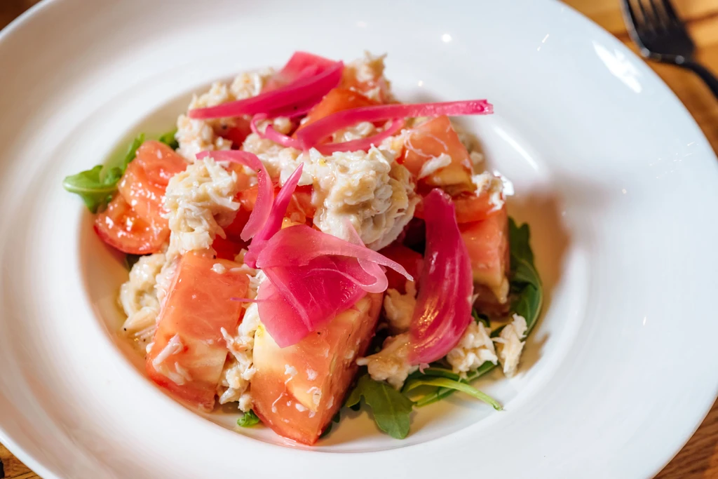 Crab salad with pink fruit, pickled onions, and leafy greens.