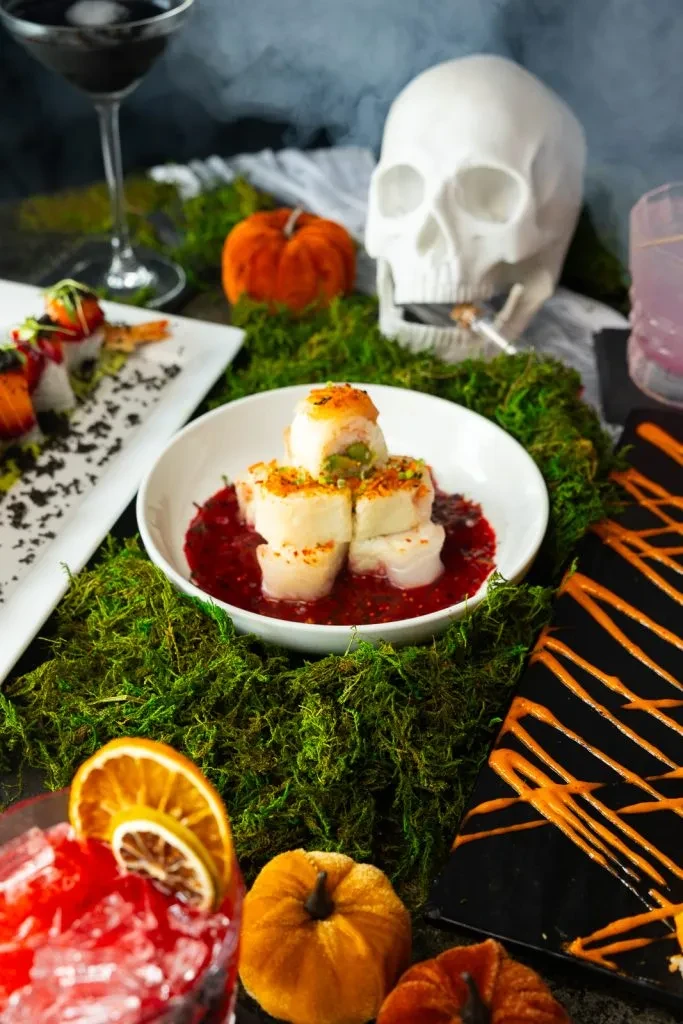 Halloween table with scallops, sushi, cocktails, pumpkins, and smoking skull.