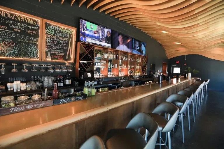 Sleek, modern bar with stools, stocked back bar, and TVs displaying sports.