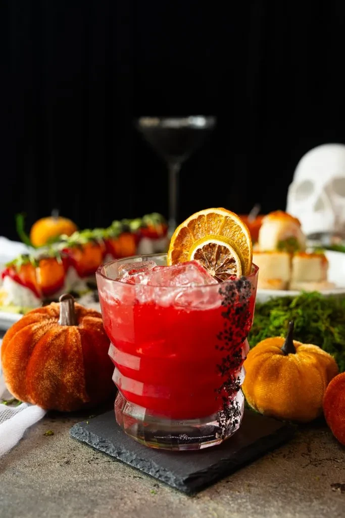 Red cocktail, textured glass, black sprinkles, dried orange, Halloween setting.