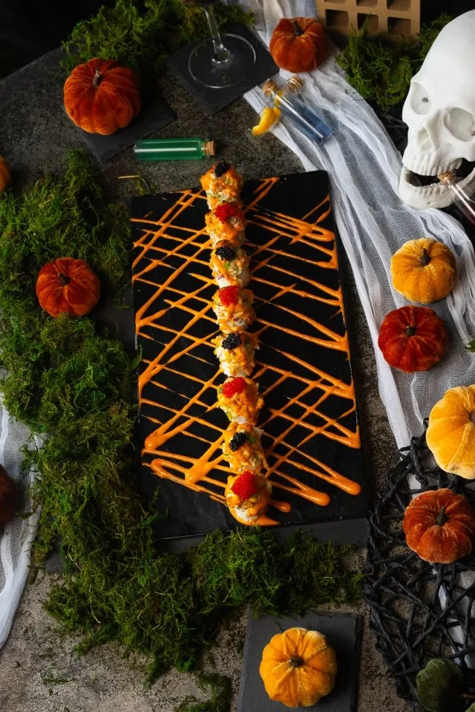Halloween sushi rolls with roe, orange drizzle, spooky decorations.