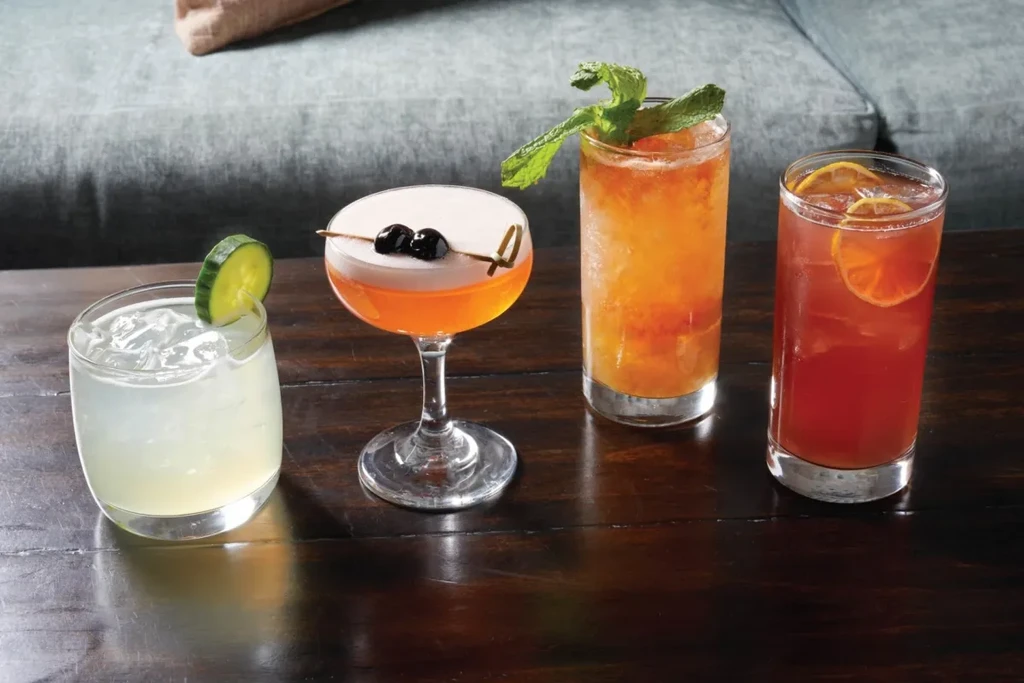 Four different garnished cocktails on a dark wood bar setting.