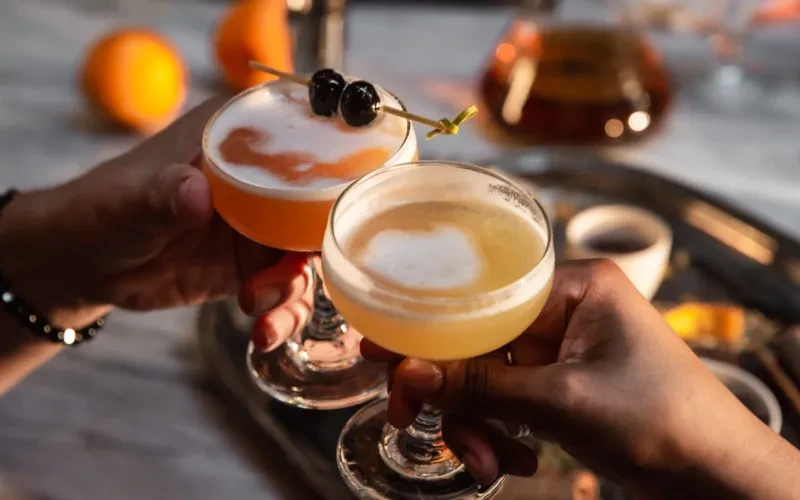 Two orange and yellow frothy cocktails held up for a toast.