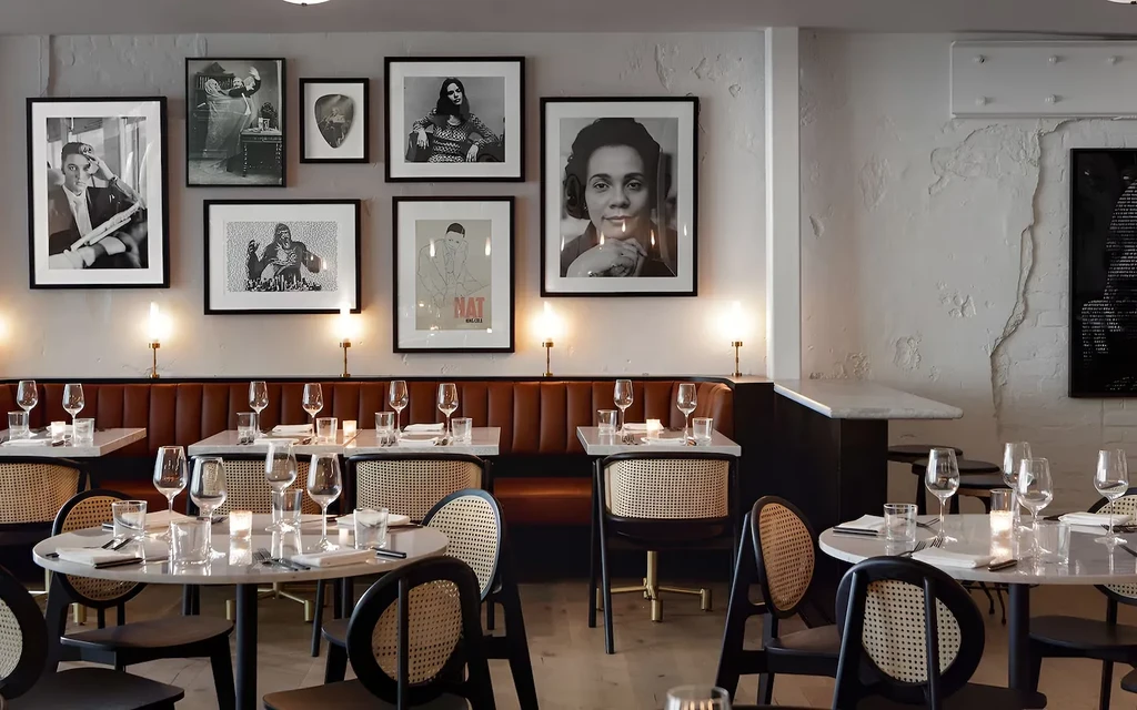 Elegant restaurant interior with set tables, leather banquette, and gallery wall.