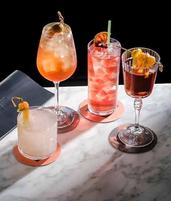 Four garnished cocktails on white marble against a dark background.
