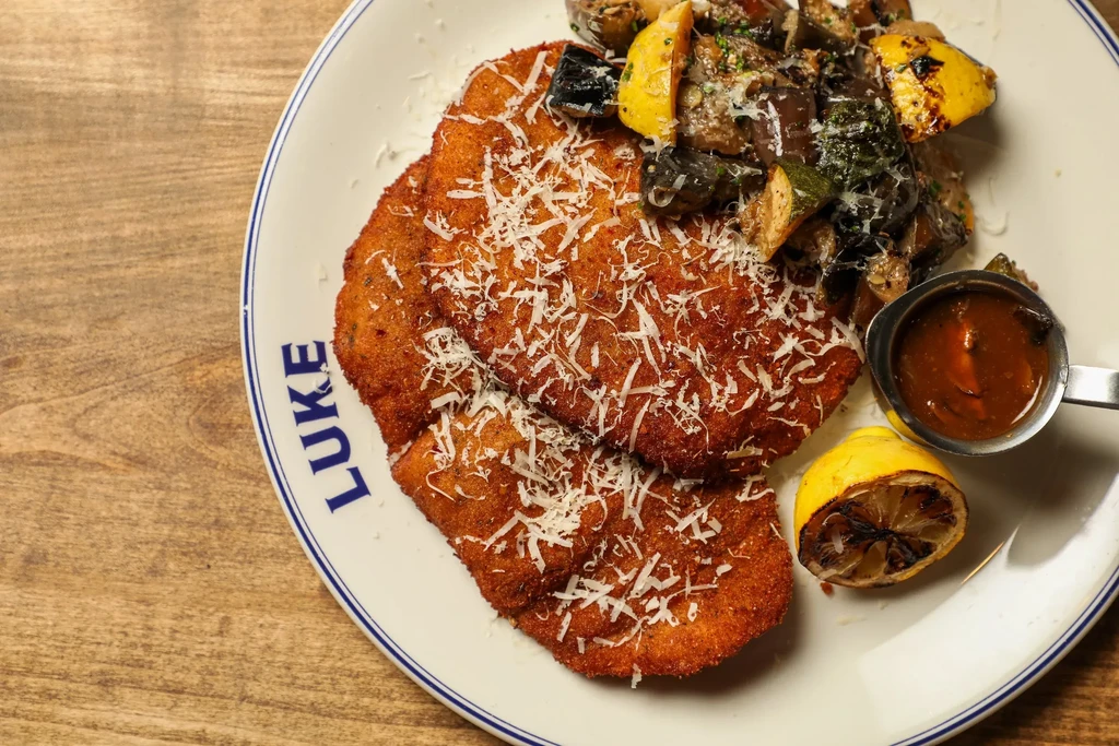 Plate of cheesy schnitzel, roasted vegetables, sauce, and grilled lemon.