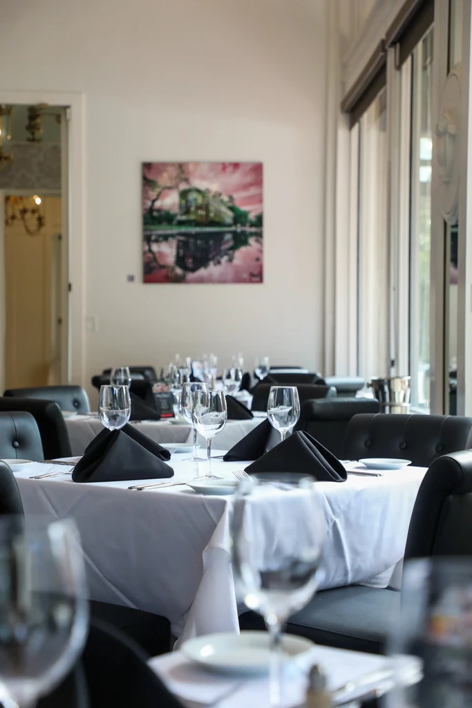 Empty restaurant dining room, set tables, black chairs, landscape art.