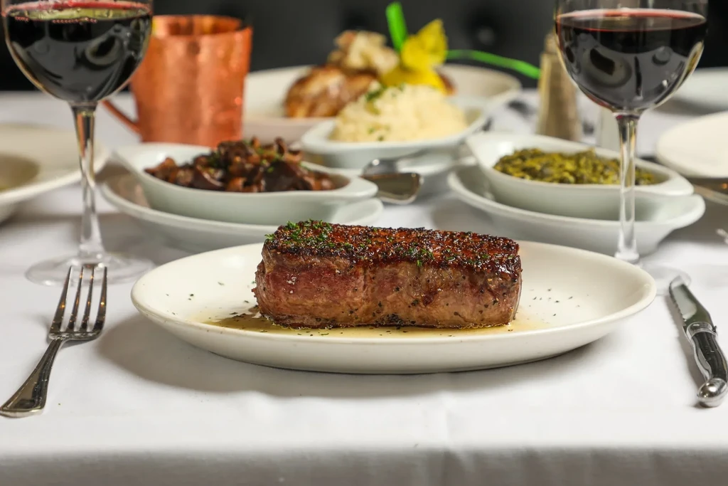 Seared steak, red wine, and side dishes on an elegant dining table.