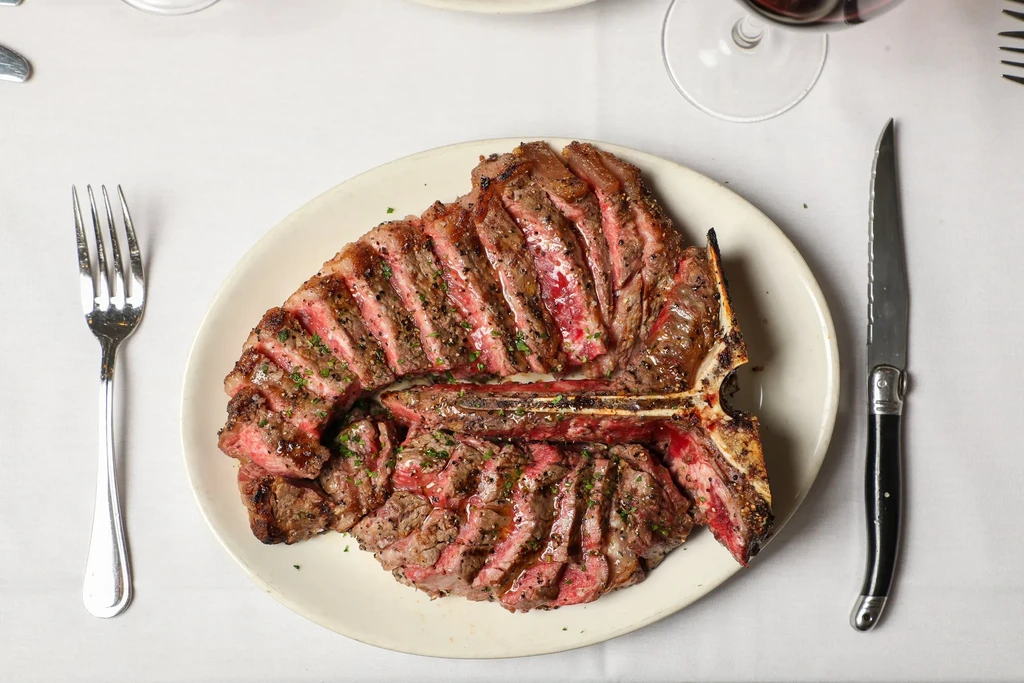 Medium-rare T-bone steak, sliced and seasoned, with cutlery and red wine.