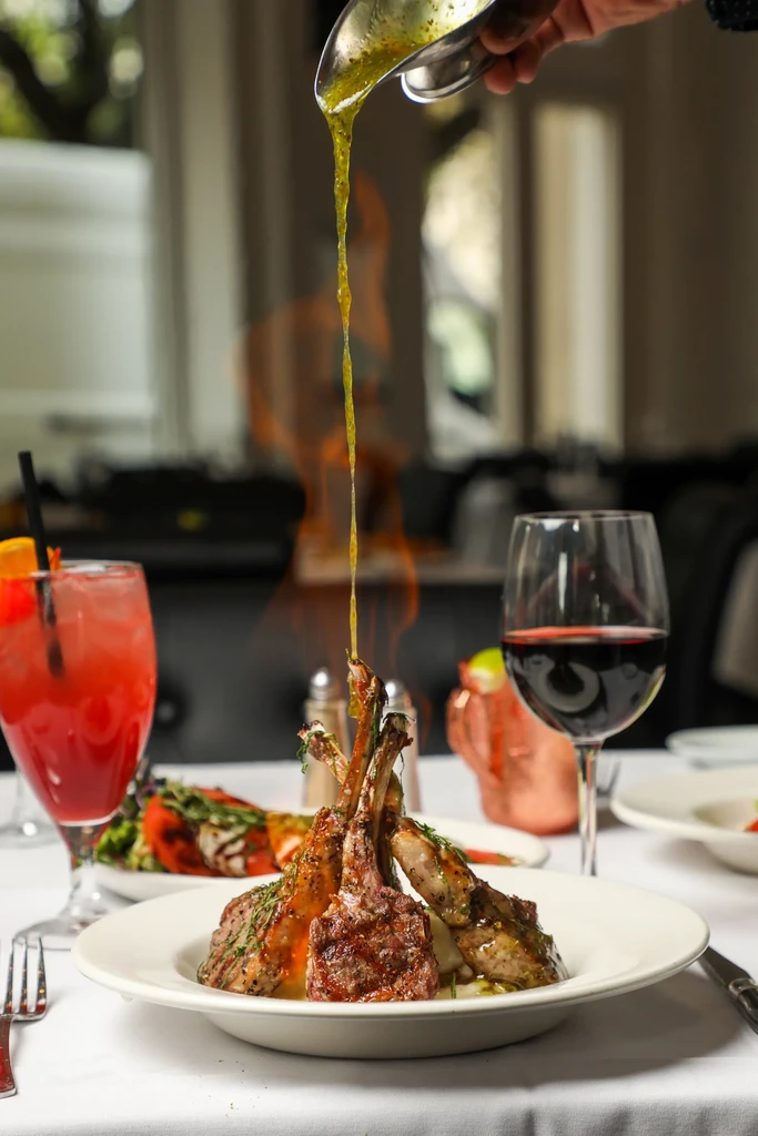 Sauce poured from ladle over flaming lamb chops in elegant restaurant.