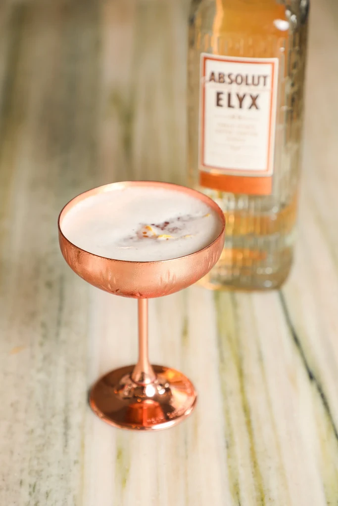 Frothy cocktail in hammered copper glass, Absolut Elyx vodka in background.