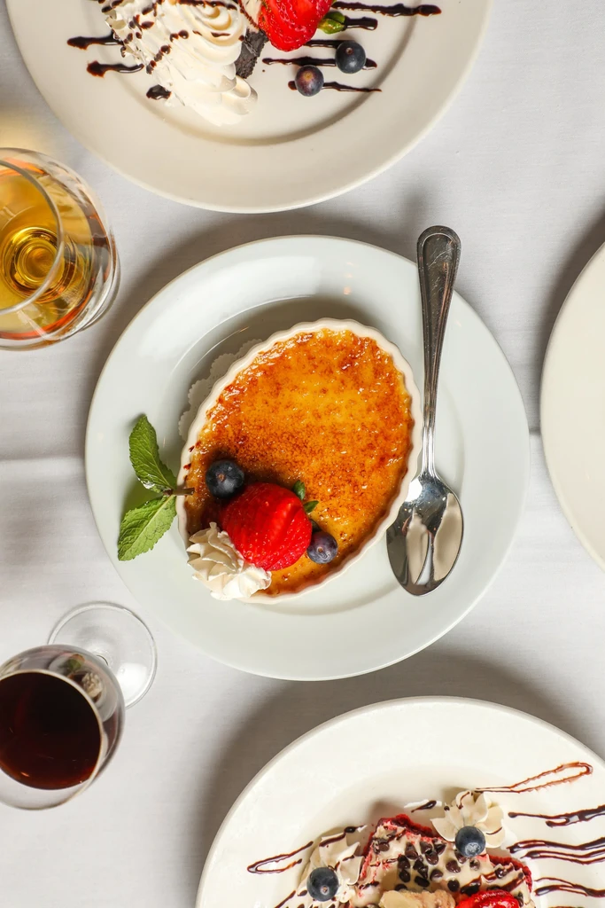 Overhead view of crème brûlée, other desserts, and drinks on a white table.