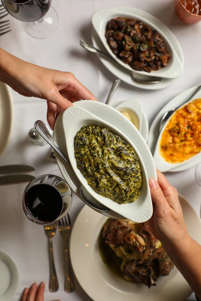 Two pairs of hands pass creamed spinach at a table with shared dishes.