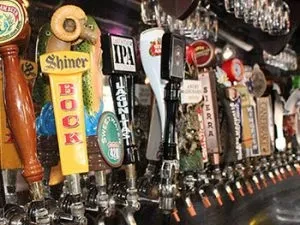 Row of various branded beer tap handles behind a dim bar.