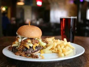 Close-up of a large burger, golden fries, and a dark drink.