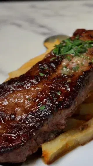Seared steak with grill marks and herbs on golden french fries.