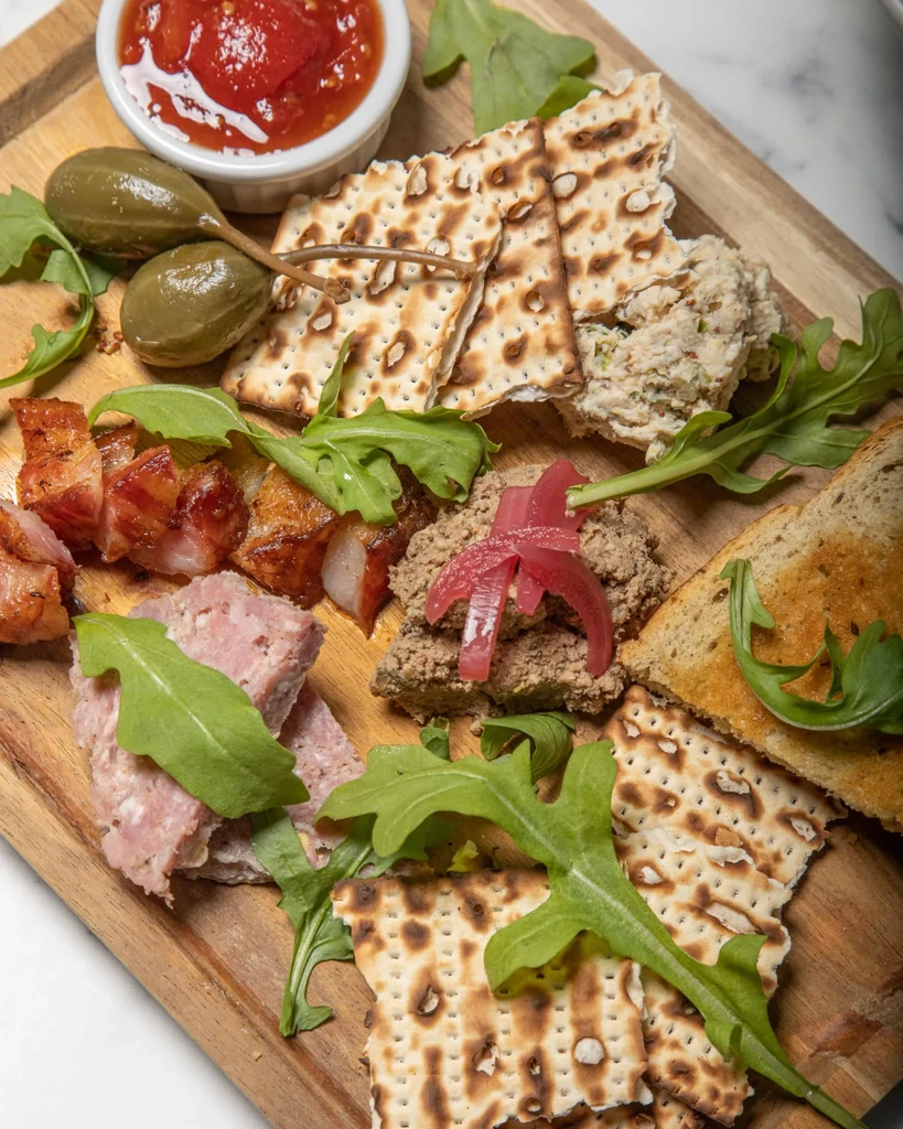Rustic wooden board with diverse appetizers: spreads, meats, and crackers.
