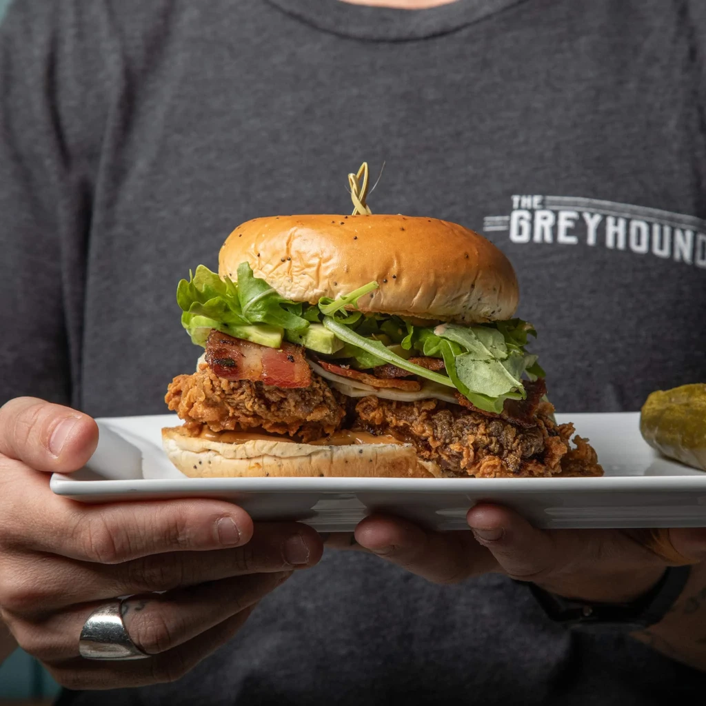 Crispy fried chicken sandwich with bacon, avocado, lettuce, and a pickle.