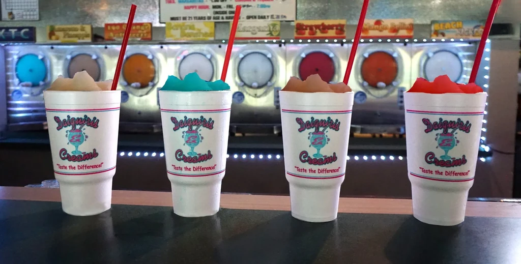 Four colorful frozen daiquiris in cups on a bar.