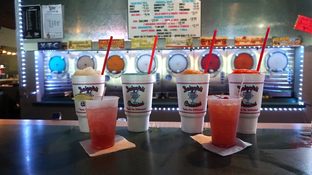 Colorful frozen drinks, machines, and a menu board on a bar counter.