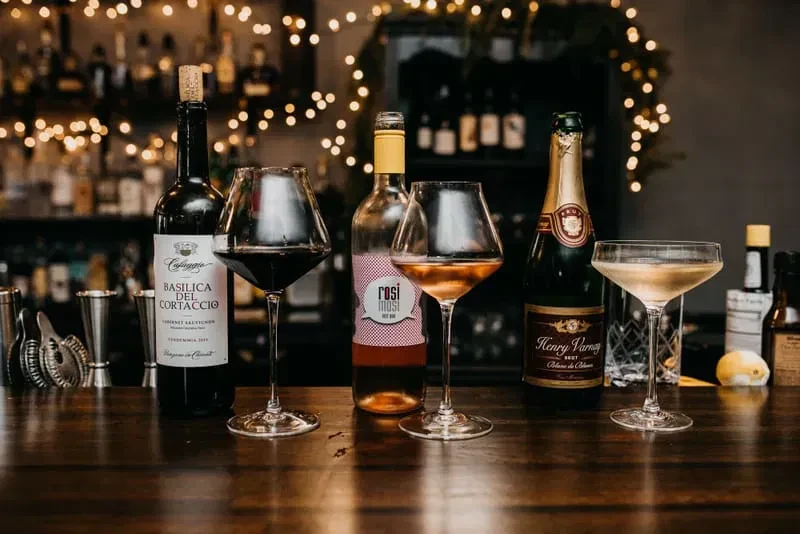 Red and rosé wine, champagne, and cocktails on a wooden bar.