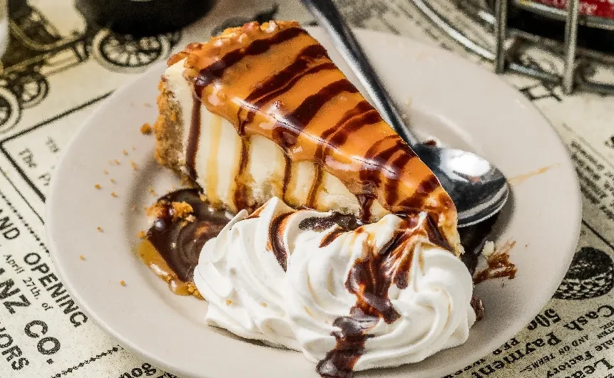 Cheesecake slice with caramel, chocolate, whipped cream, on vintage newspaper background.