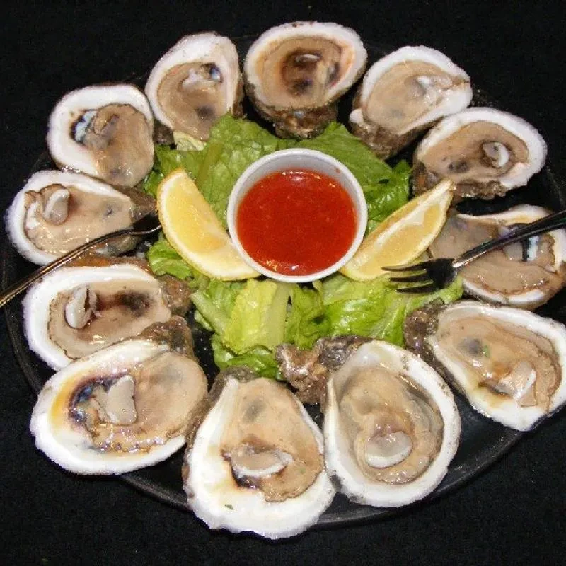 Platter of raw oysters on the half shell with cocktail sauce and lemon.