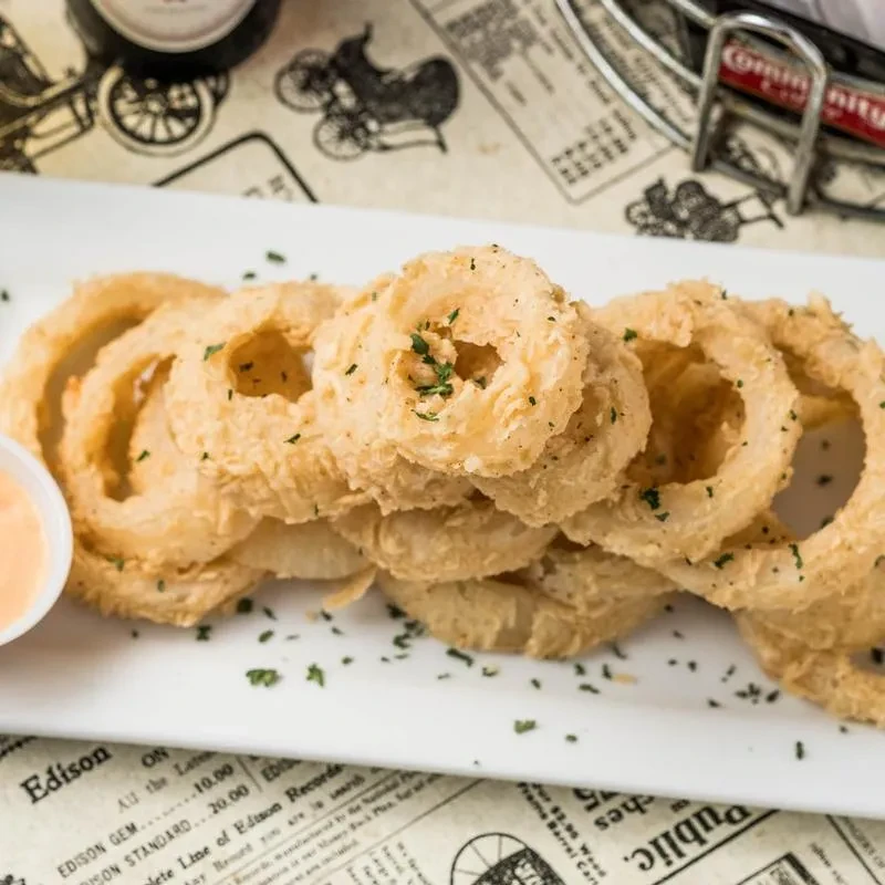 Crispy golden onion rings with dipping sauce and a vintage background.